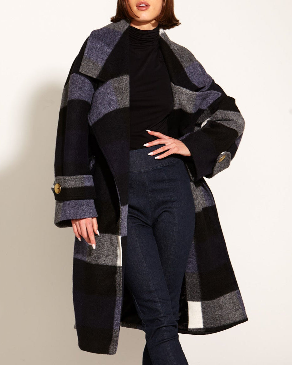 Woman wearing a long, patterned coat over a black outfit on a white background