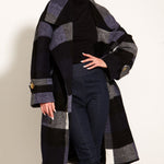 Woman wearing a long, patterned coat over a black outfit on a white background